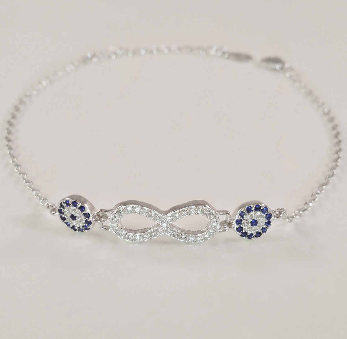 925 STERLING SILVER BRACELET WITH ETERNITY SYMBOL AND DOUBLE EVIL EYE CHARM PAVED WITH SPARKLING CZ CRYSTALS.